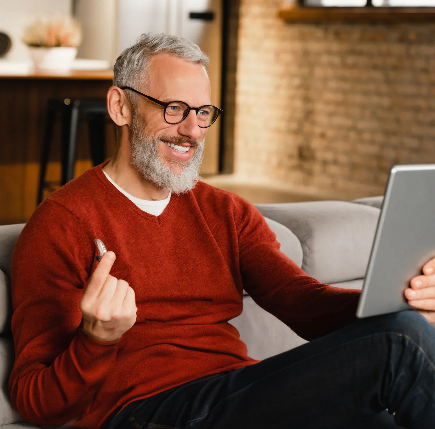 Uomo sorridente con barba grigia che fa il gesto OK mentre utilizza un tablet.